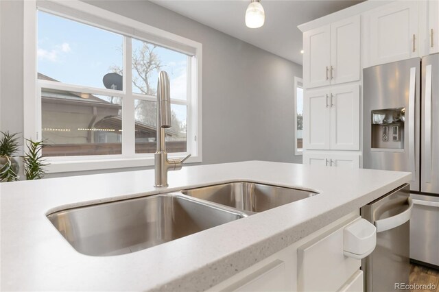 kitchen with light countertops, stainless steel refrigerator with ice dispenser, a sink, and white cabinetry