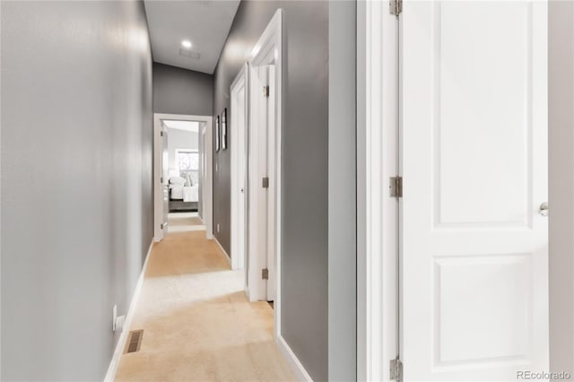 corridor featuring light colored carpet, visible vents, and baseboards