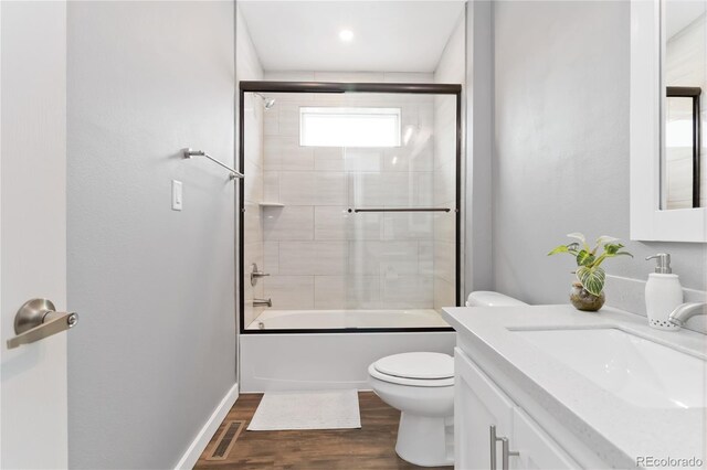 bathroom with visible vents, toilet, wood finished floors, combined bath / shower with glass door, and vanity