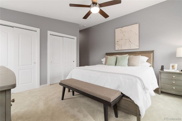 bedroom featuring ceiling fan, multiple closets, and light colored carpet