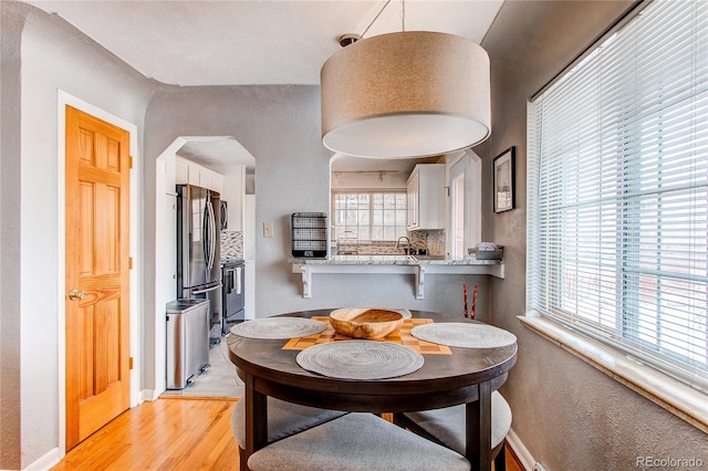 dining space with arched walkways, light wood-type flooring, a wealth of natural light, and baseboards