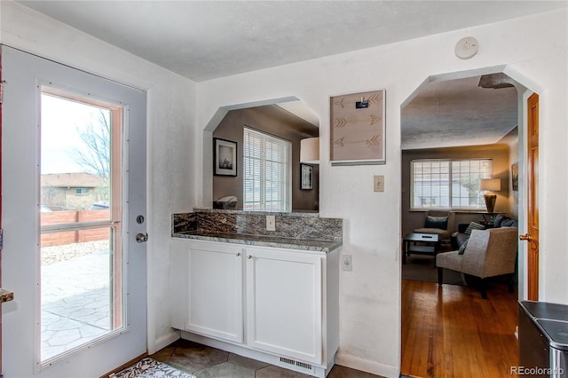 kitchen featuring visible vents, stone counters, wood finished floors, arched walkways, and white cabinetry