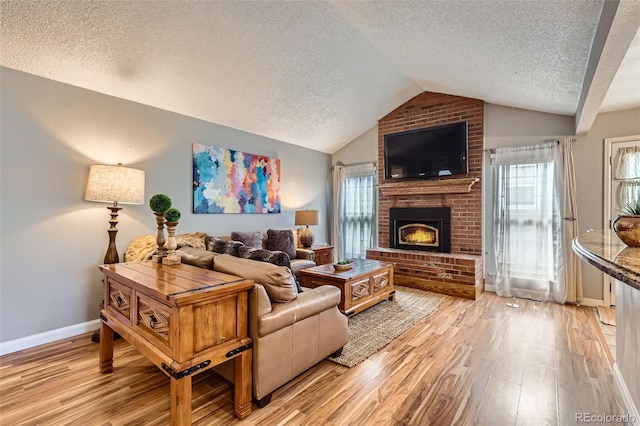 living room featuring lofted ceiling, light wood finished floors, a textured ceiling, and a fireplace