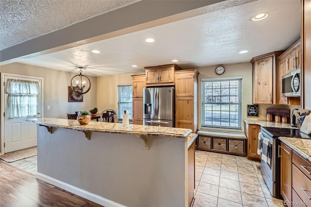 kitchen with a center island with sink, appliances with stainless steel finishes, a textured ceiling, a kitchen bar, and recessed lighting