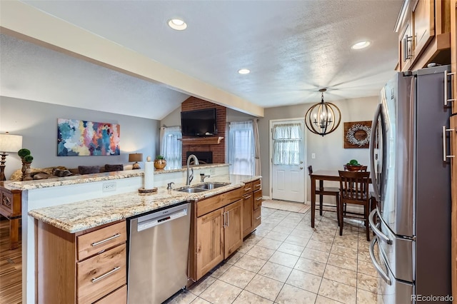 kitchen with appliances with stainless steel finishes, open floor plan, hanging light fixtures, light stone countertops, and a sink