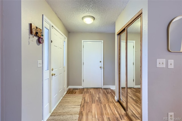 entryway featuring a textured ceiling, light wood-style flooring, and baseboards