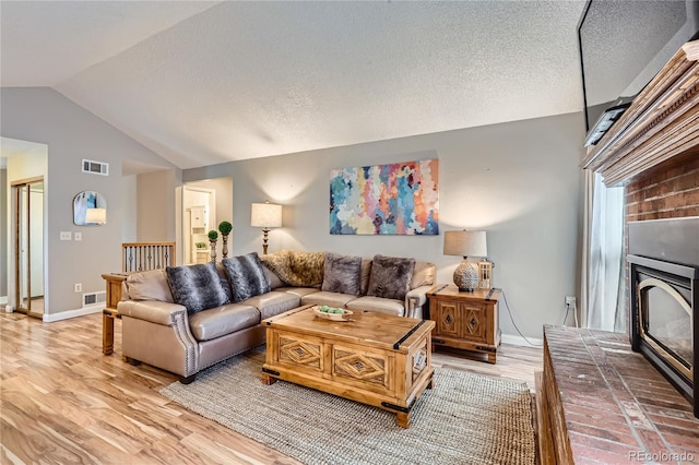 living room with light wood-style floors, a brick fireplace, visible vents, and vaulted ceiling