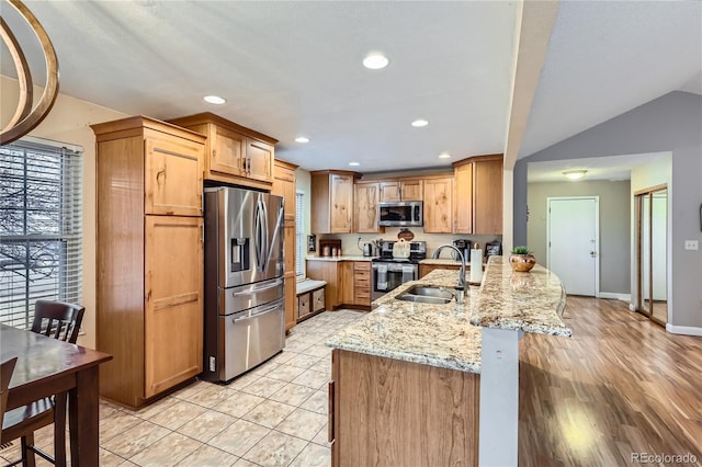 kitchen featuring light stone counters, a peninsula, a breakfast bar, a sink, and appliances with stainless steel finishes