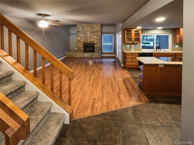 living room with dark wood-type flooring, ceiling fan, a stone fireplace, and sink