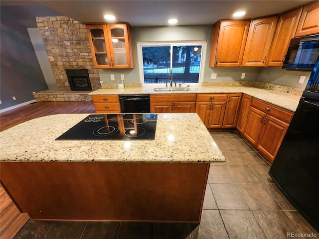 kitchen with sink, a kitchen island, a fireplace, light stone countertops, and black appliances