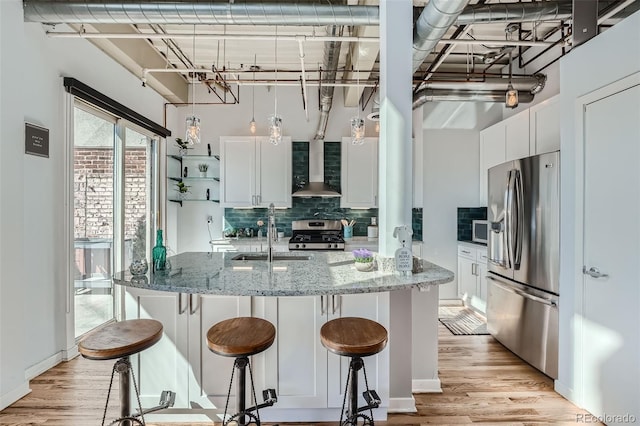 kitchen with wall chimney range hood, light stone countertops, appliances with stainless steel finishes, and white cabinetry