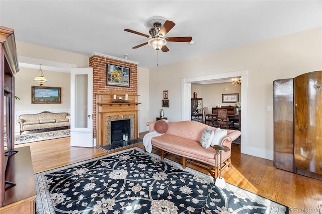 living area with a brick fireplace, wood finished floors, baseboards, and ceiling fan