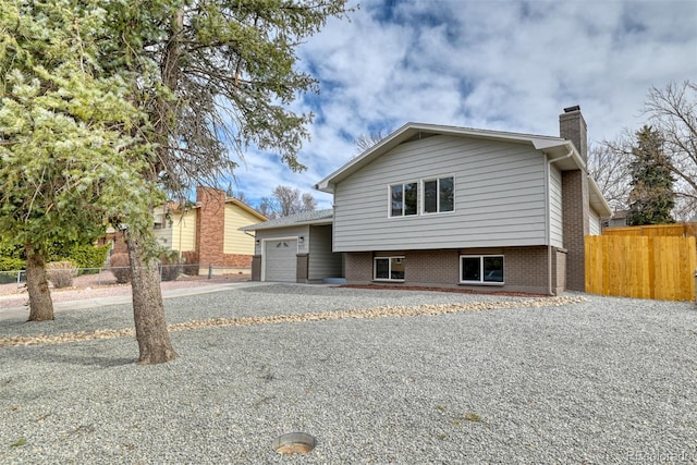 tri-level home featuring brick siding, fence, a chimney, a garage, and driveway