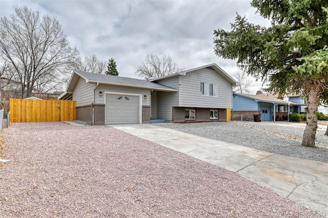 tri-level home featuring driveway, brick siding, an attached garage, and fence