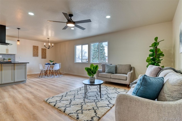 living room with baseboards, light wood-style floors, ceiling fan with notable chandelier, and a textured ceiling