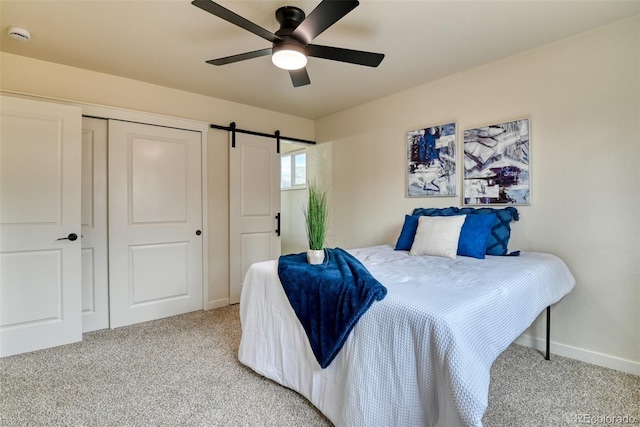 bedroom with carpet, baseboards, ceiling fan, a closet, and a barn door