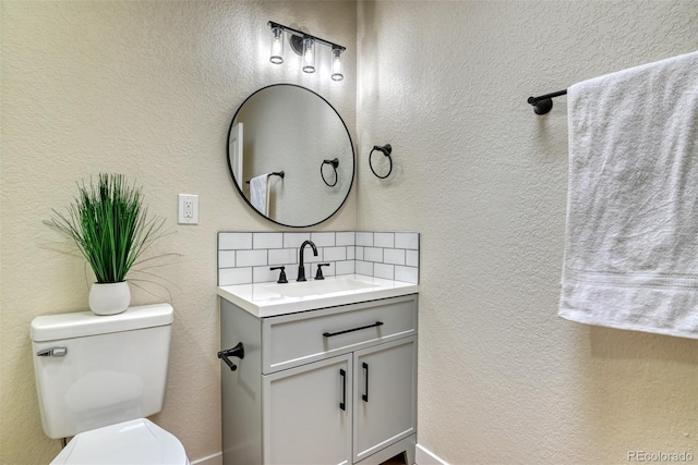 bathroom featuring tasteful backsplash, toilet, vanity, and a textured wall