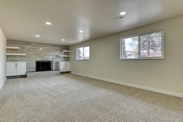 unfurnished living room featuring baseboards, visible vents, a textured ceiling, carpet flooring, and a large fireplace