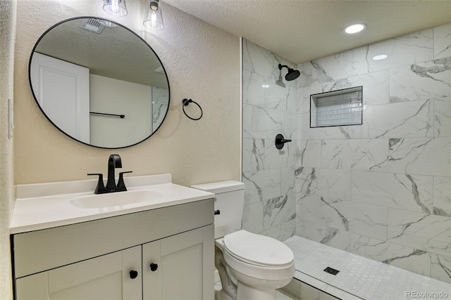 bathroom with toilet, a textured ceiling, tiled shower, vanity, and a textured wall