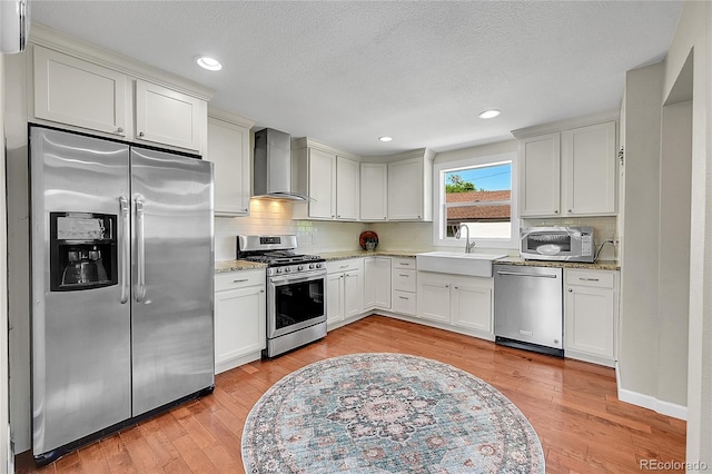 4268 S Delaware St, Englewood, CO 80110 - kitchen featuring appliances with stainless steel finishes, wall chimney range hood, backsplash, light wood-style floors, and light stone counters
