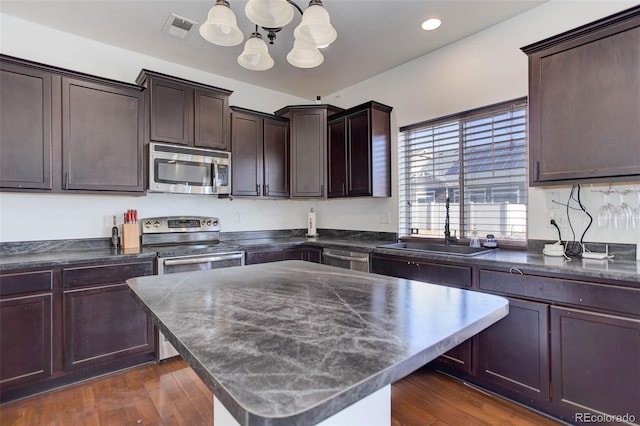 kitchen featuring appliances with stainless steel finishes, pendant lighting, sink, dark brown cabinets, and dark wood-type flooring