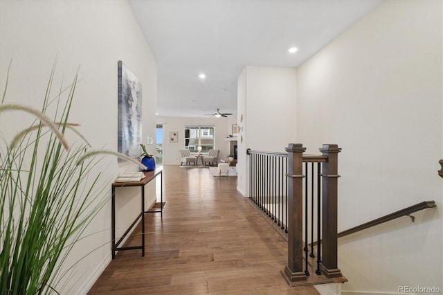 corridor with baseboards, wood finished floors, an upstairs landing, and recessed lighting