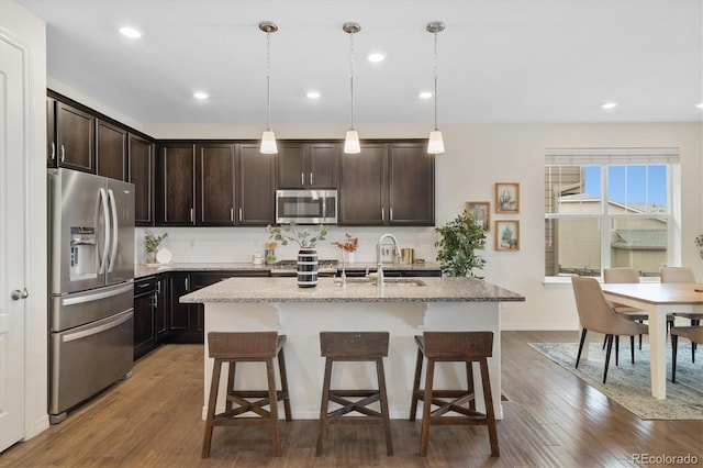 kitchen with dark brown cabinetry, a breakfast bar area, wood finished floors, stainless steel appliances, and a sink