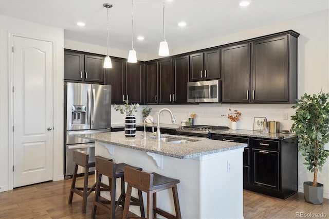 kitchen with light wood-style flooring, decorative backsplash, appliances with stainless steel finishes, a sink, and light stone countertops