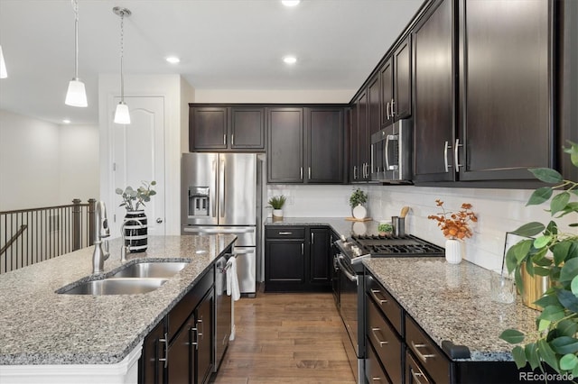 kitchen featuring dark wood finished floors, decorative backsplash, appliances with stainless steel finishes, a sink, and an island with sink