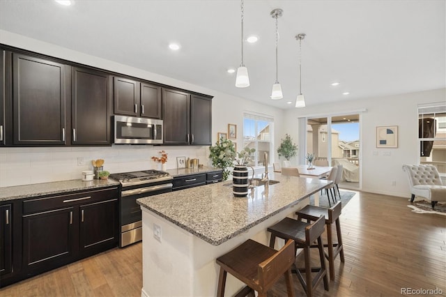 kitchen with stainless steel appliances, light stone counters, a breakfast bar area, and light wood-style floors