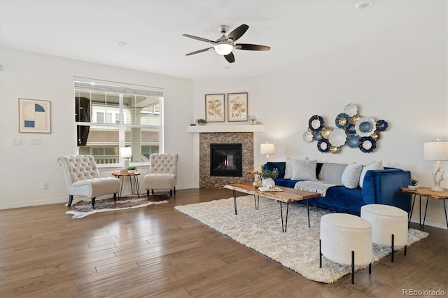 living room featuring ceiling fan, a fireplace, baseboards, and wood finished floors