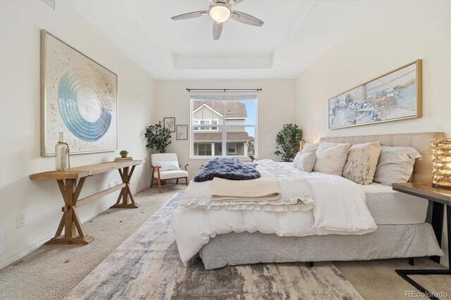 carpeted bedroom featuring ceiling fan, a raised ceiling, and baseboards