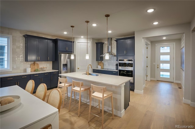 kitchen featuring appliances with stainless steel finishes, a kitchen breakfast bar, an island with sink, decorative light fixtures, and wall chimney exhaust hood