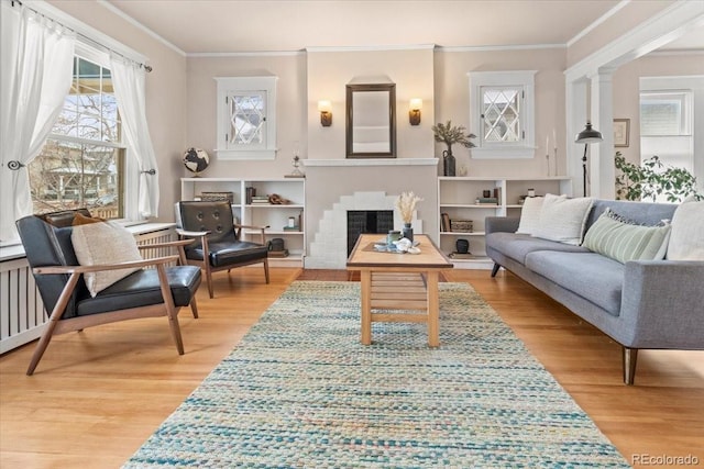 living area with ornamental molding, light hardwood / wood-style floors, a brick fireplace, and ornate columns