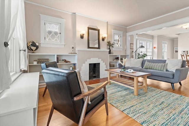 sitting room with a brick fireplace, crown molding, wood-type flooring, and decorative columns