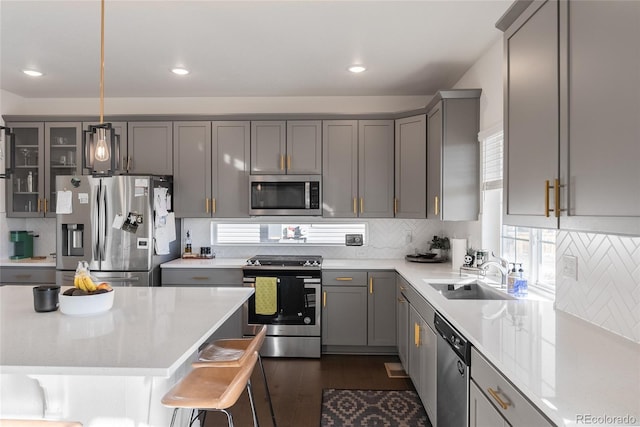 kitchen featuring appliances with stainless steel finishes, a kitchen breakfast bar, hanging light fixtures, sink, and gray cabinets