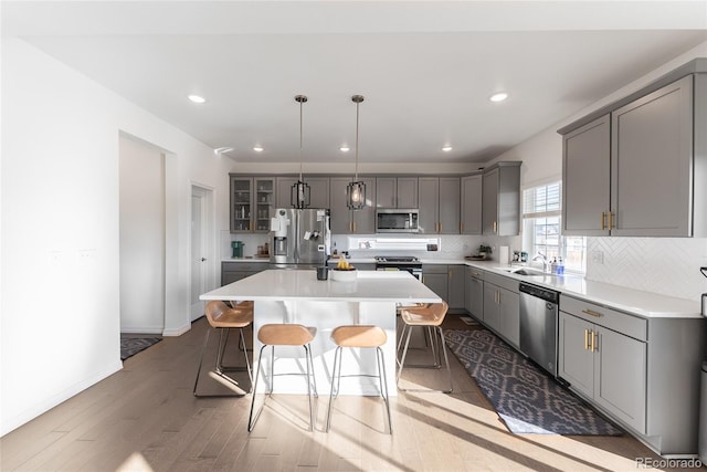 kitchen featuring pendant lighting, a kitchen island, a kitchen bar, stainless steel appliances, and gray cabinetry