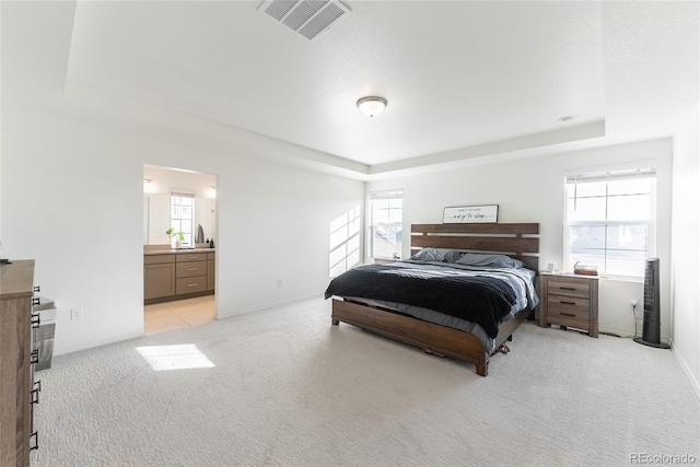 bedroom featuring ensuite bathroom, a raised ceiling, and light carpet