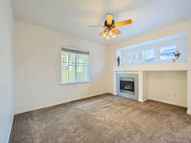 unfurnished living room with a tiled fireplace, a wealth of natural light, ceiling fan, and carpet flooring