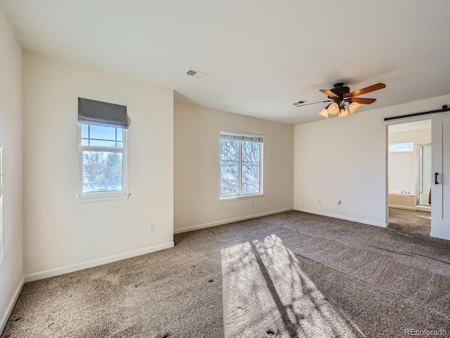 empty room with carpet floors, plenty of natural light, a barn door, and ceiling fan