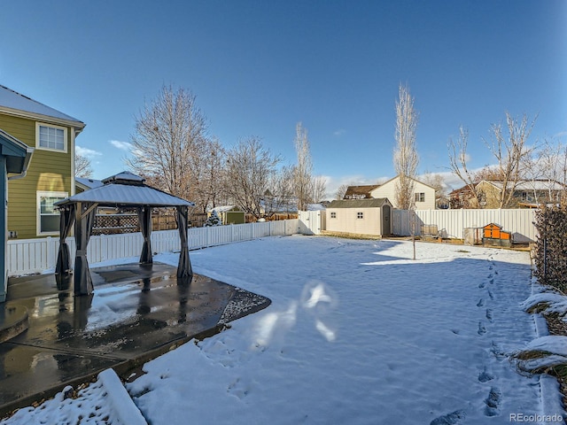 yard covered in snow with a gazebo and a storage unit