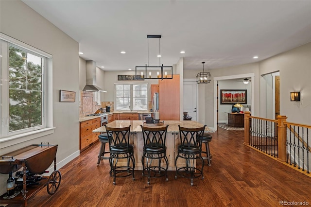 kitchen with wall chimney range hood, recessed lighting, a breakfast bar area, dark wood-style floors, and baseboards