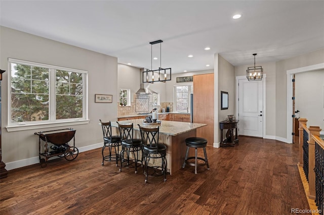 kitchen with an inviting chandelier, recessed lighting, light stone countertops, dark wood-type flooring, and a kitchen bar