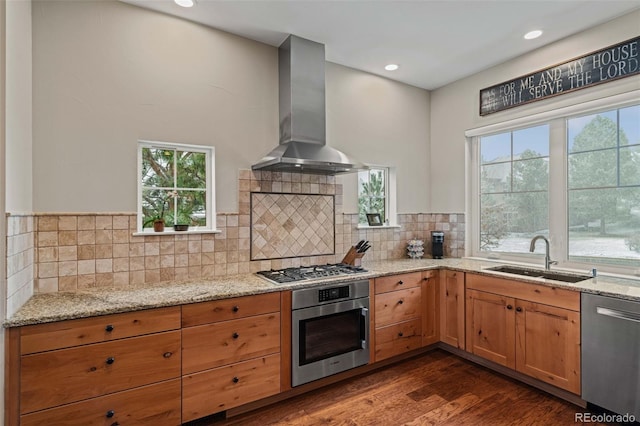 kitchen with a sink, appliances with stainless steel finishes, wall chimney exhaust hood, and light stone counters
