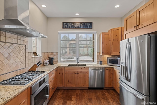 kitchen with dark wood-style flooring, light stone counters, wall chimney range hood, stainless steel appliances, and a sink