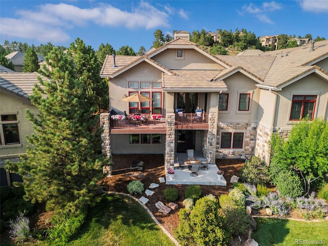 rear view of property featuring a tile roof, stone siding, a patio, and stucco siding