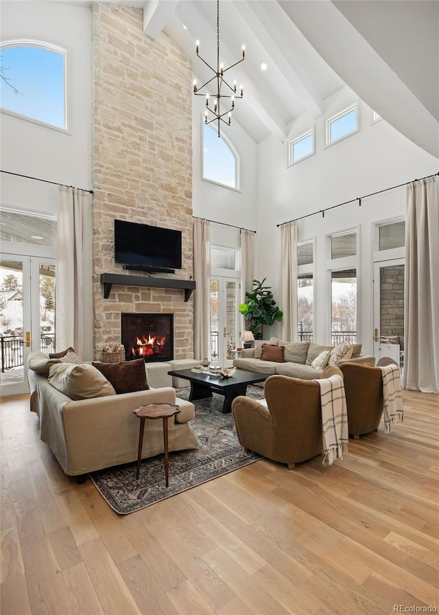 living room featuring an inviting chandelier, high vaulted ceiling, beamed ceiling, a fireplace, and light hardwood / wood-style floors