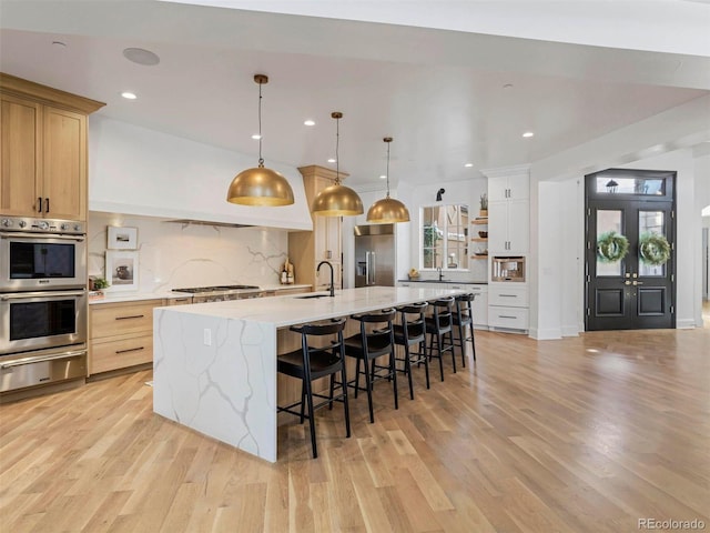 kitchen featuring appliances with stainless steel finishes, pendant lighting, white cabinetry, a large island, and light stone countertops