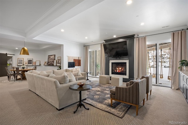 carpeted living room featuring crown molding, a large fireplace, and a barn door