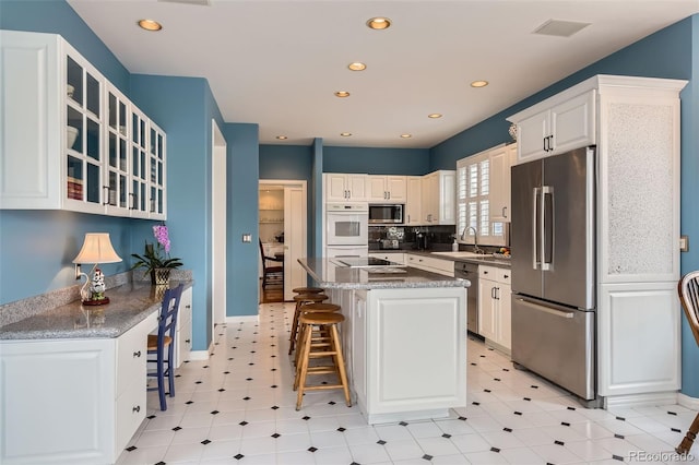 32 Silver Fox Cir, Greenwood Village, CO 80121 - kitchen with stainless steel appliances, a sink, a breakfast bar, white cabinets, and recessed lighting